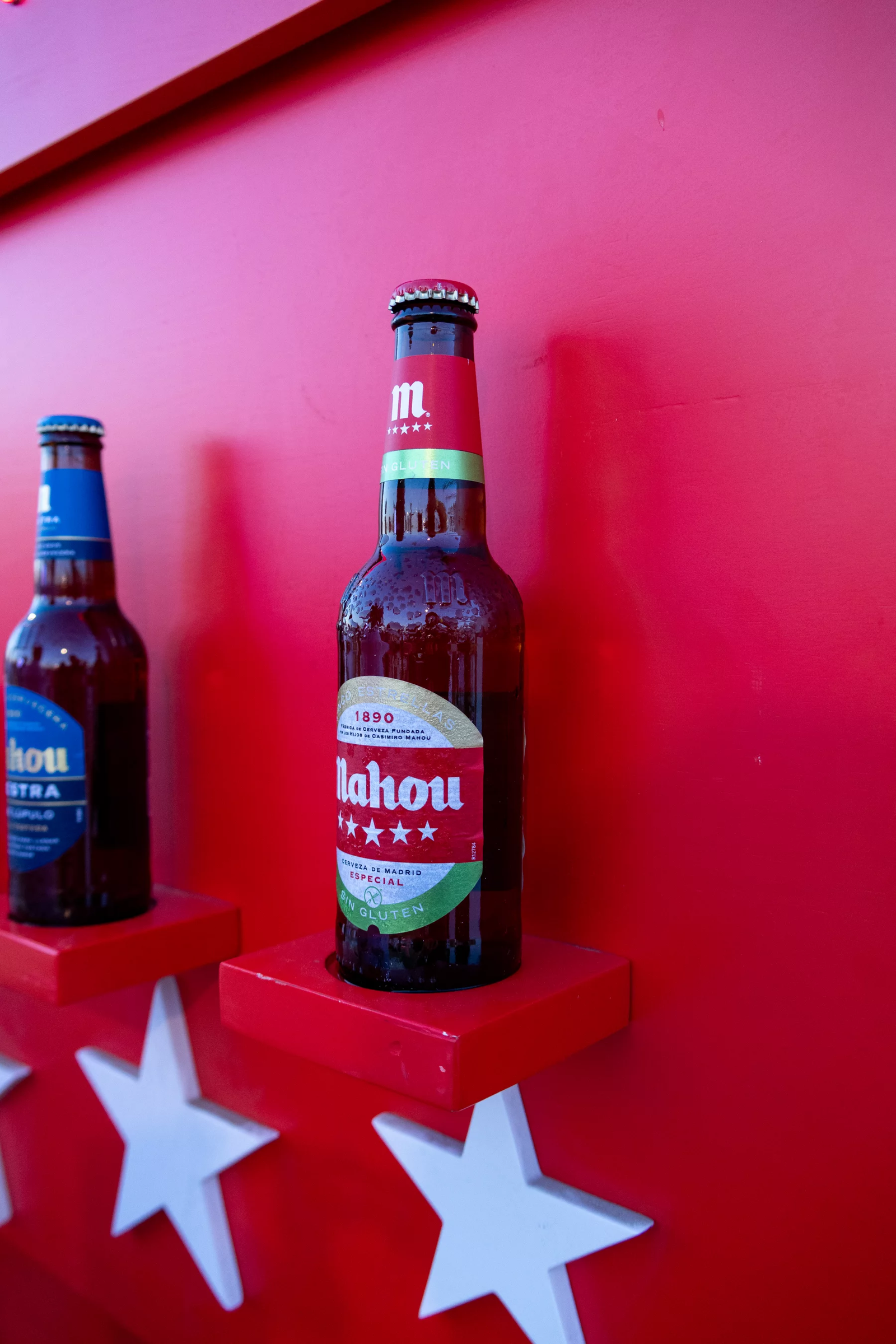 Botellas de Mahou expuestas en baldas con estrellas blancas sobre una pared roja en Amarilla Night