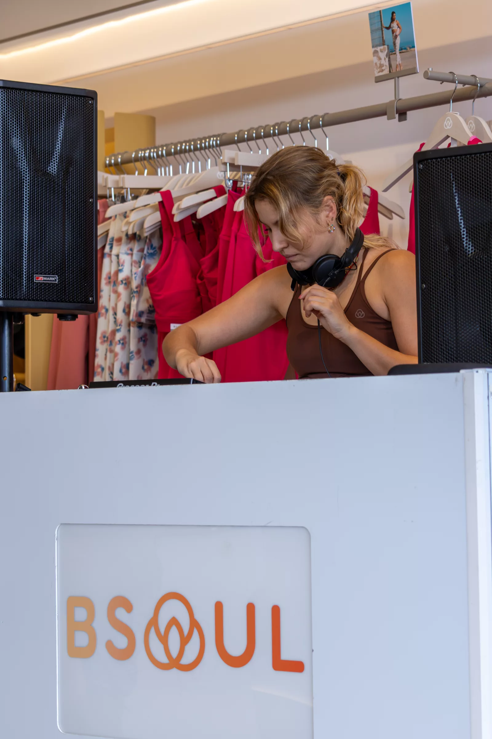 DJ con auriculares pinchando en una cabina con el logotipo de BSOUL, delante de perchas de ropa