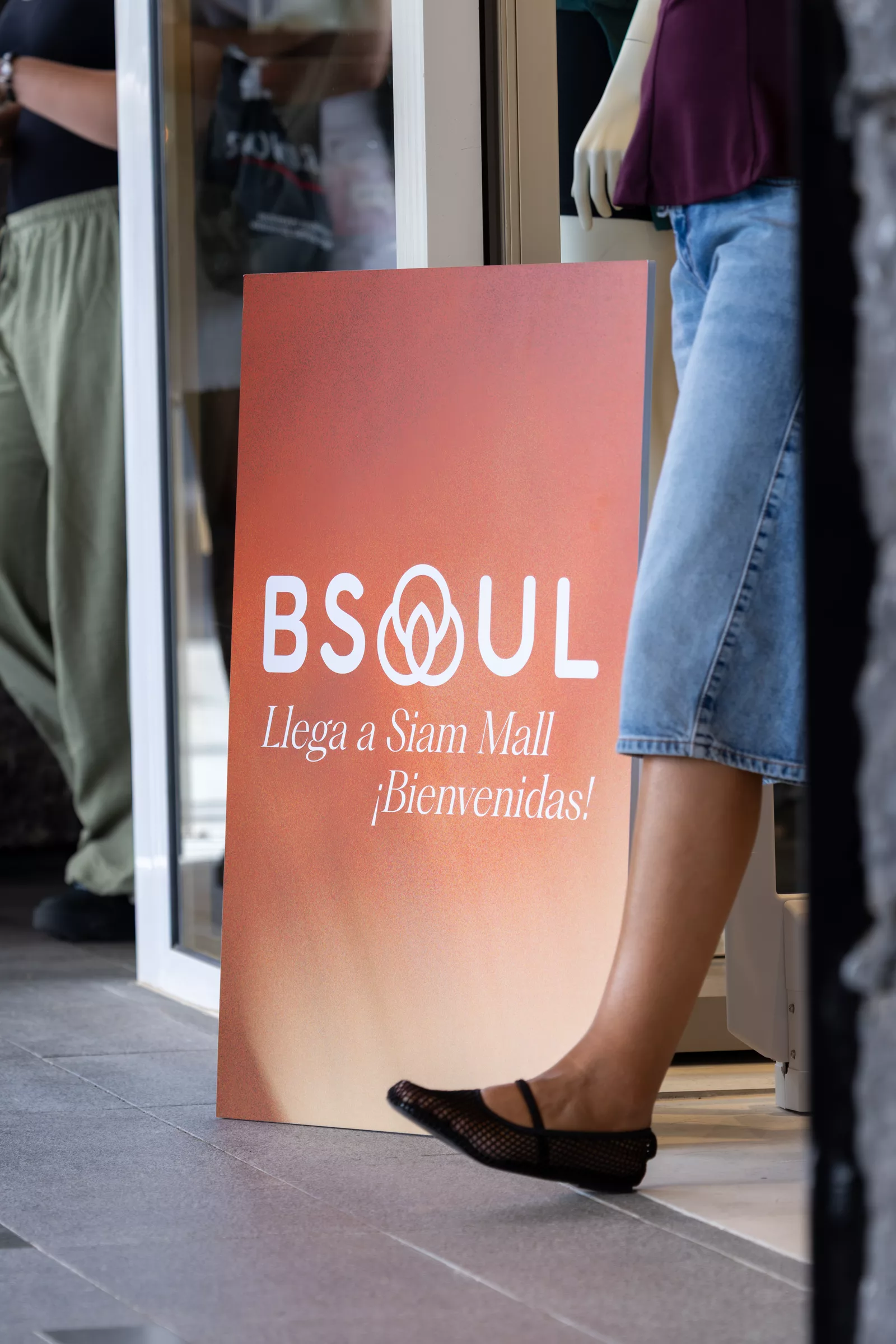 Cartel de BSOUL en la entrada de la tienda con el texto «Llega a Siam Mall ¡Bienvenidas!», con clientas entrando
