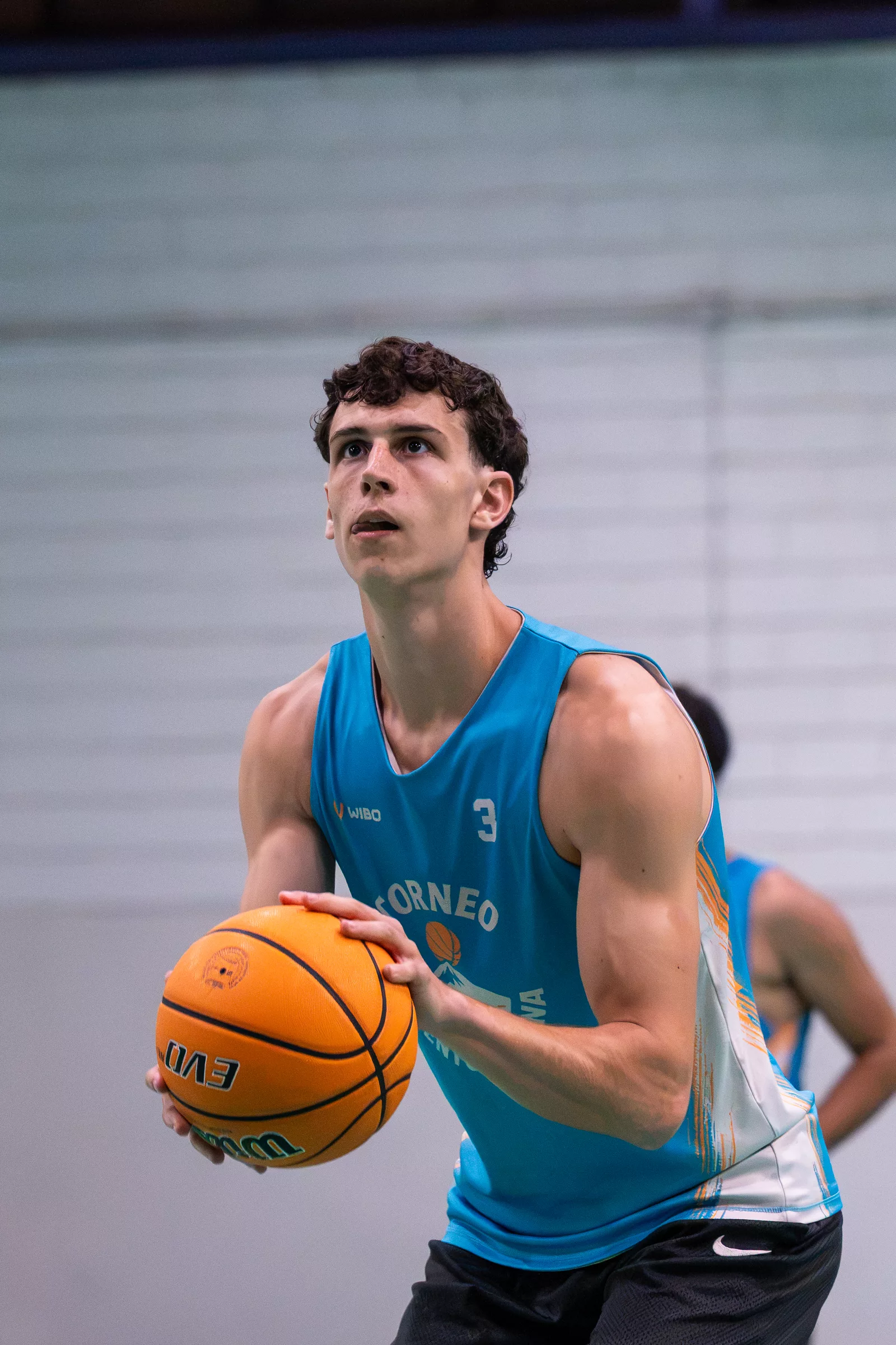 Jugador con camiseta azul y el dorsal 3 sujeta el balón y mira al aro antes de lanzar