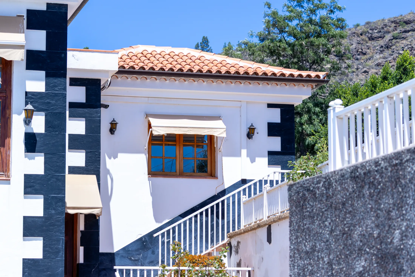 Fachada blanca con esquinas de piedra oscura, escalera y ventana de madera en Finca Viñas